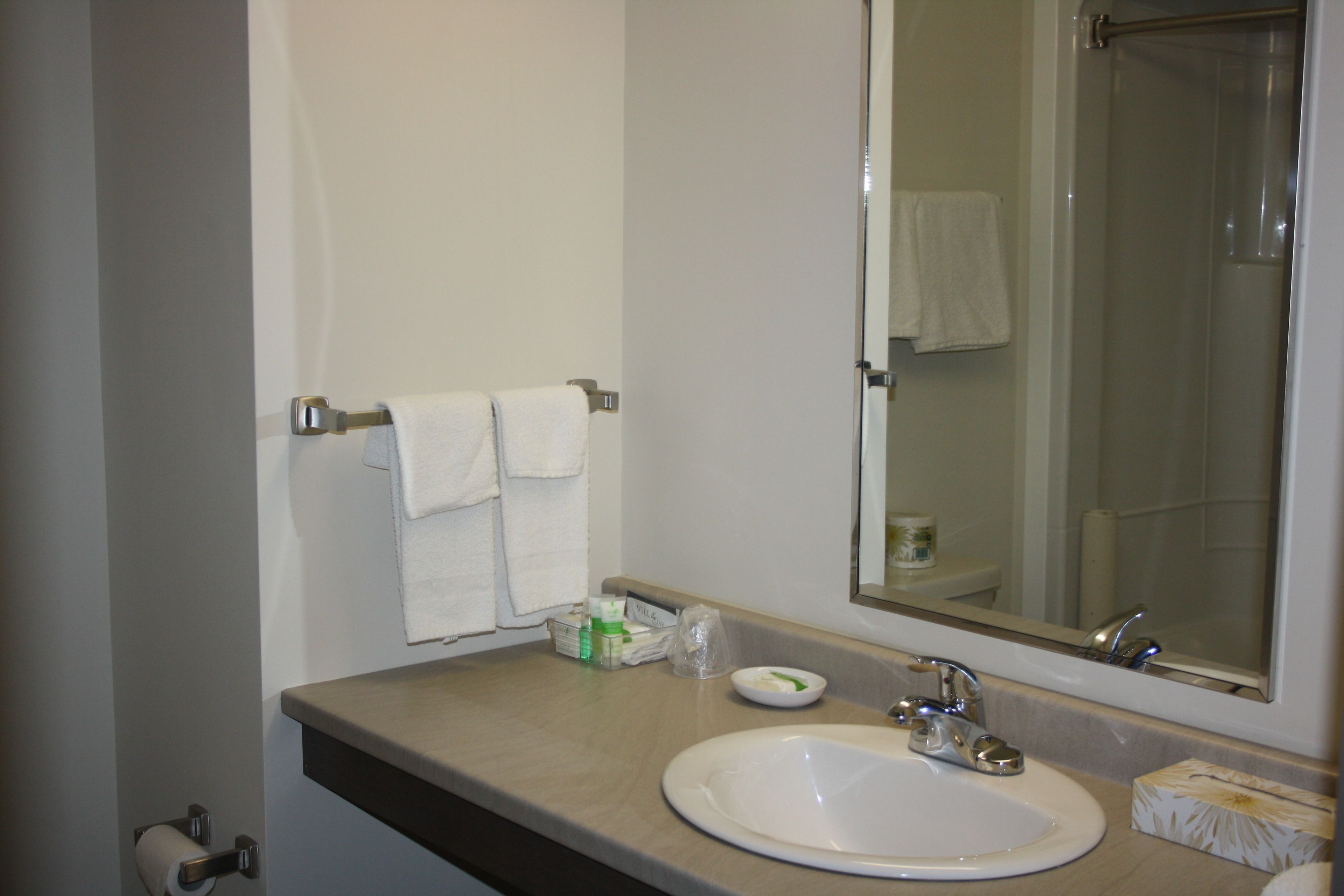 A bathroom with a sink, mirror, towel rack, and a shower visible in the reflection.