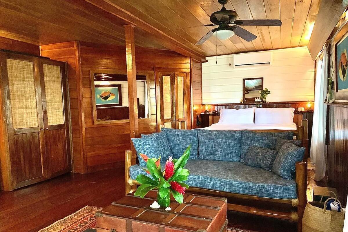 A wooden-floored living room with a sofa, a wooden chest, and a ceiling fan.