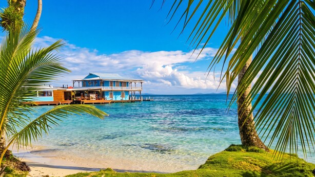 A beachfront property with a wooden dock, a blue building with a white roof, and clear blue water. - Casa Acuario (Bocas del Toro)