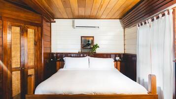 Una cama con estructura de madera y ropa de cama blanca, un aire acondicionado montado en la pared y un cuadro enmarcado encima.