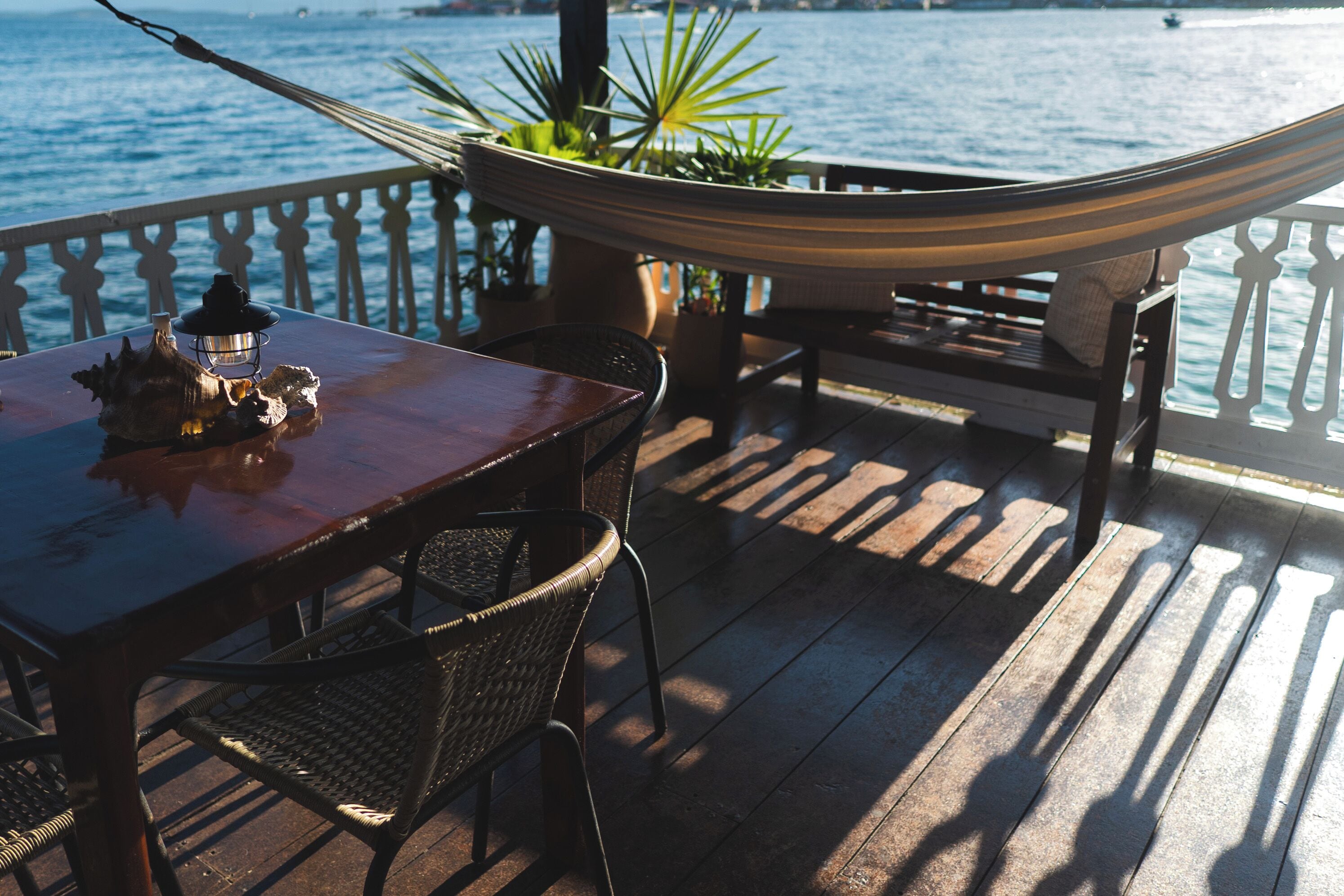 A wooden deck with a hammock, a table with a lantern, and potted plants.