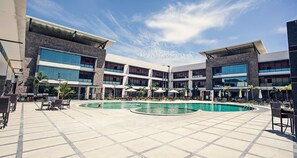 Un patio de hotel con piscina central, mobiliario exterior y varios niveles de balcones.