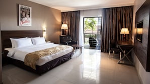 A hotel room with a large bed, two chairs, a small table, a TV, and a balcony with curtains. - Laguna Hotel (Port Moresby)
