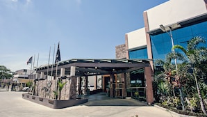A modern hotel entrance with a covered walkway, stone pillars, and a parking area. - Laguna Hotel (Port Moresby)