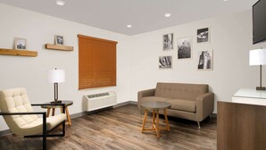 Una sala de estar moderna con un sofá color beige, un sillón color crema, una mesita redonda de madera y una lámpara de pie. Hay cuadros enmarcados en la pared y un ventanal con persianas.