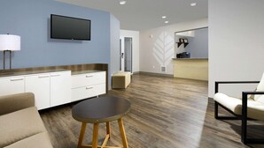 Una habitación de hotel moderna con televisión de pantalla plana, un sofá, una mesa redonda y suelo de madera.