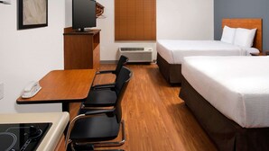 Habitación de hotel con dos camas, un escritorio con silla, televisión y ventana con persianas.