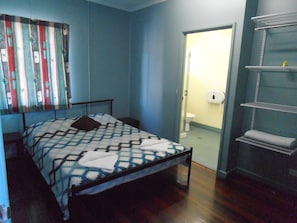 A bedroom with a bed, a door leading to a bathroom, and a shelf with towels. - Buzers (Torquay)