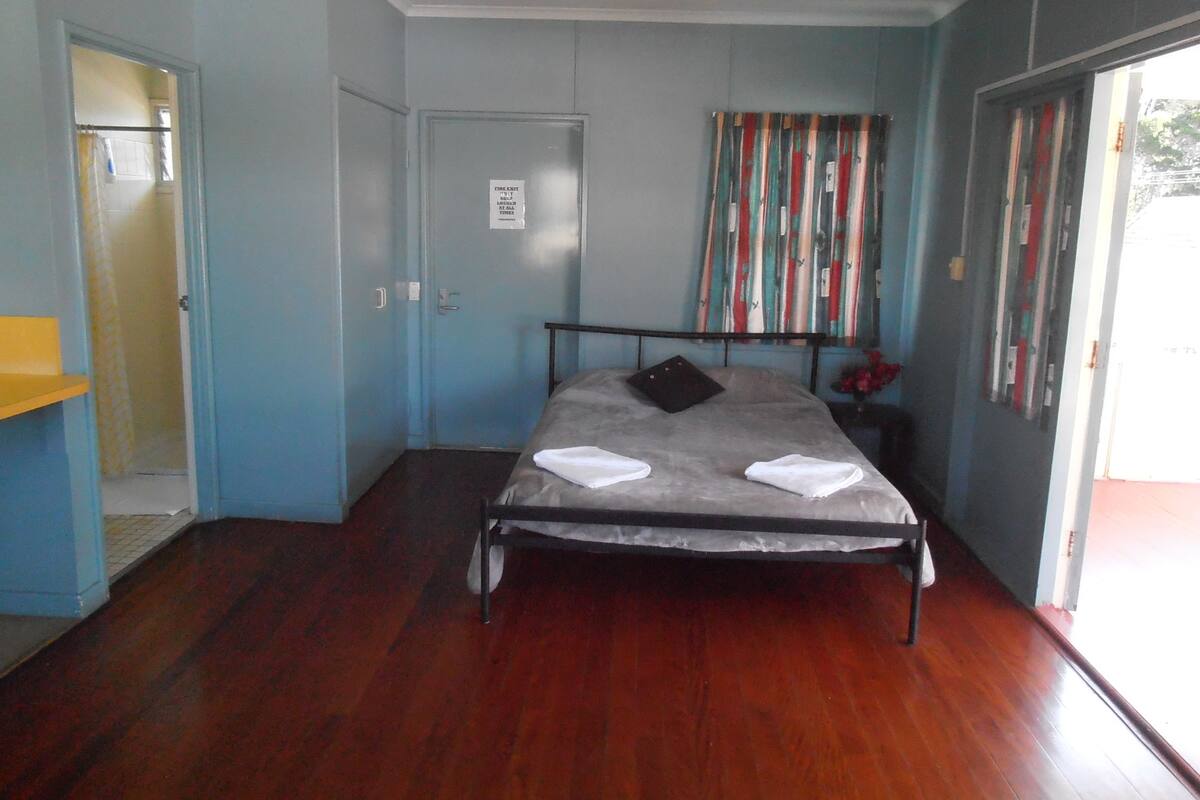 Ein Schlafzimmer mit einem Einzelbett, einem Deckenventilator, einer Tür mit Feuerausgang-Beschilderung und einem Fenster mit Vorhängen.