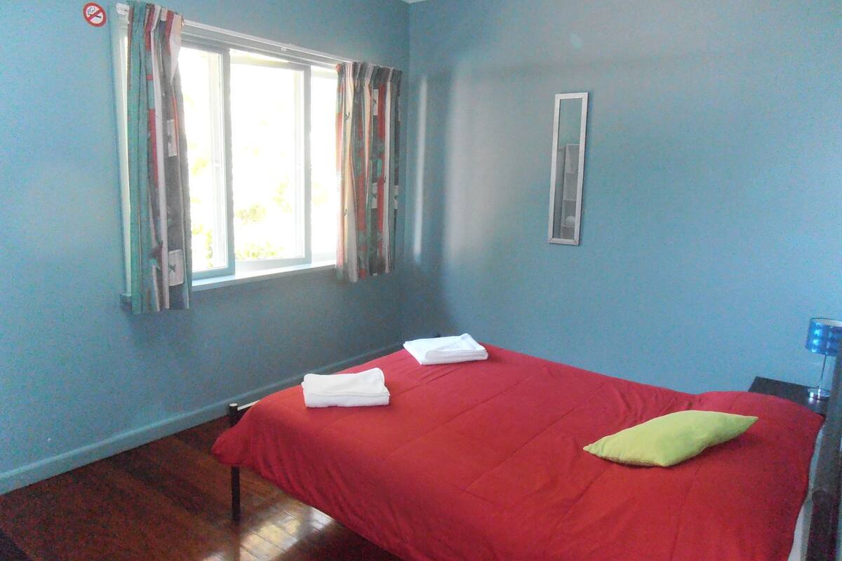 Ein Zimmer mit Bett, einem Vorhangfenster, einem Spiegel und einer blauen Wand.