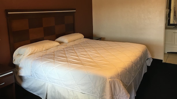 A hotel room with a bed, a nightstand, and a dresser. - Deluxe Inn Of Roswell (Roswell)