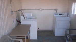 A small laundry room with a washing machine, dryer, and a table with chairs. - Deluxe Inn Of Roswell (Roswell)