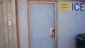 A door with a lock, a sign reading 'GUEST LAUNDRY ICE', and a trash bin to the right. - Deluxe Inn Of Roswell (Roswell)