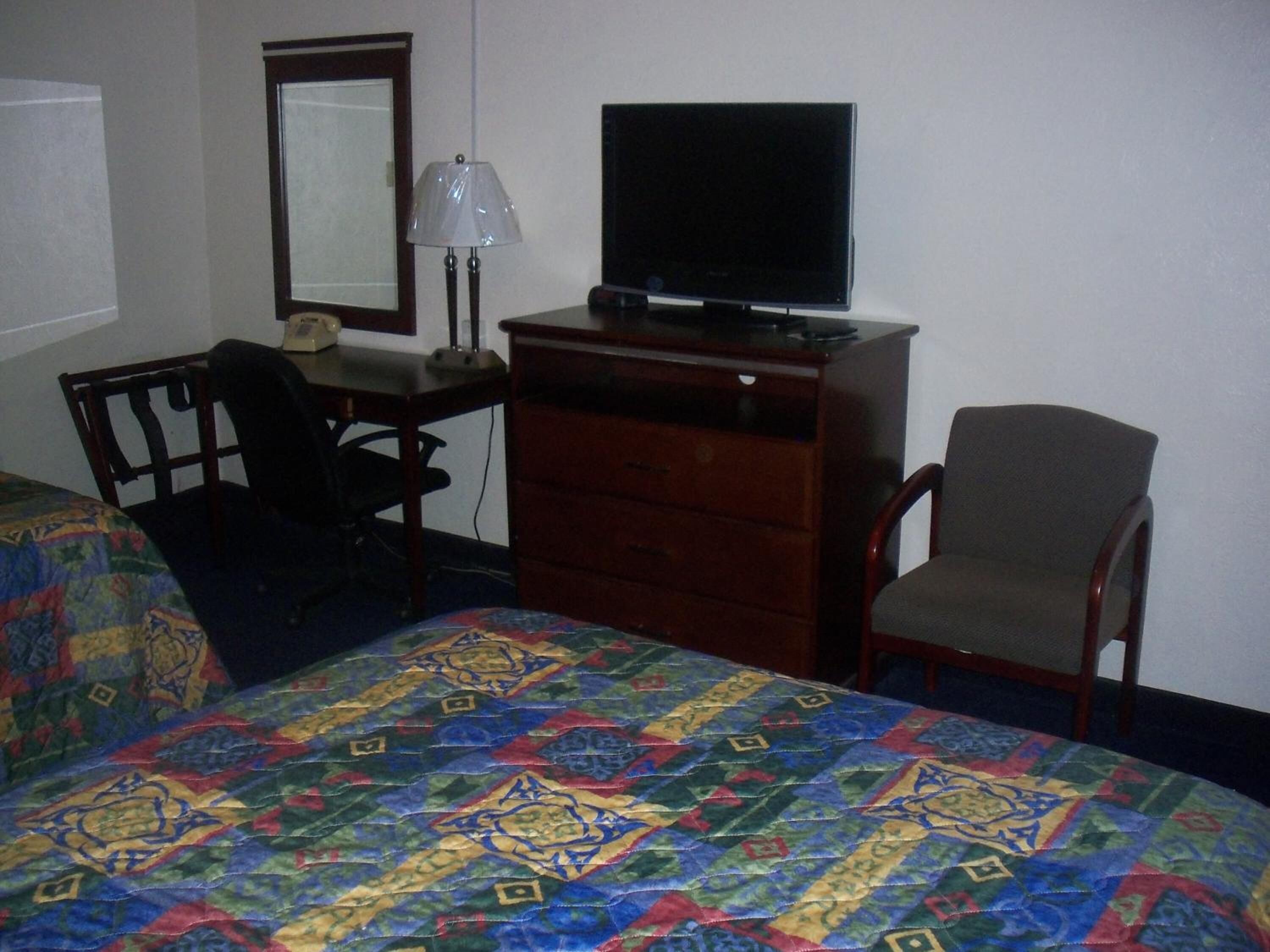 Una habitación de hotel con una cama, un escritorio con televisor, una silla y un aparador.