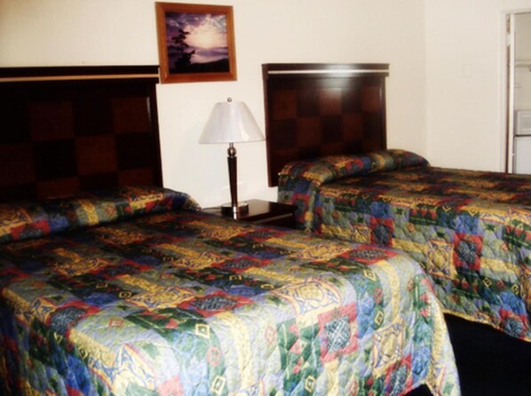 A hotel room with two beds, a nightstand, a lamp, and a painting on the wall.