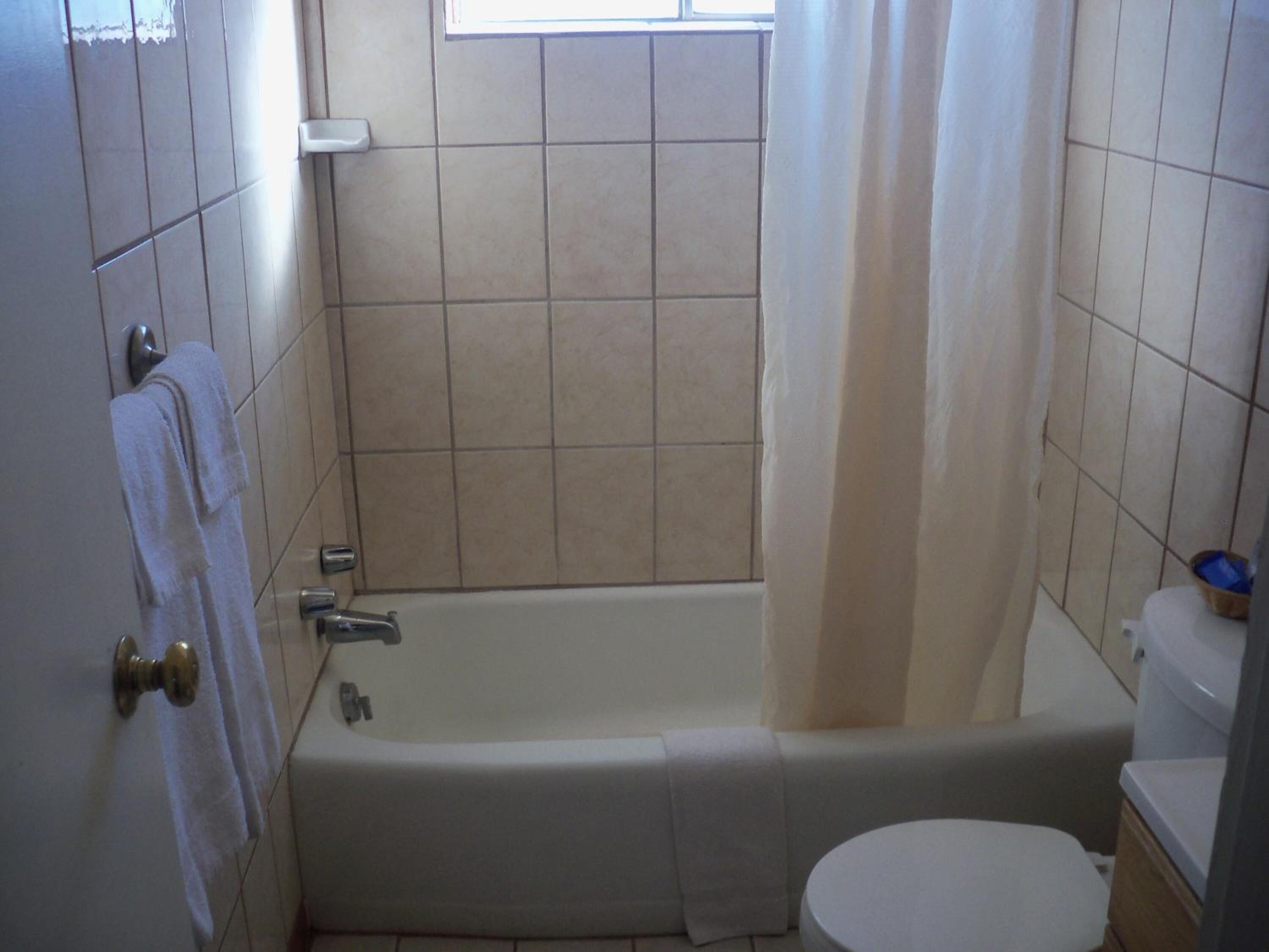 A bathroom with a bathtub, toilet, and a window with a curtain.