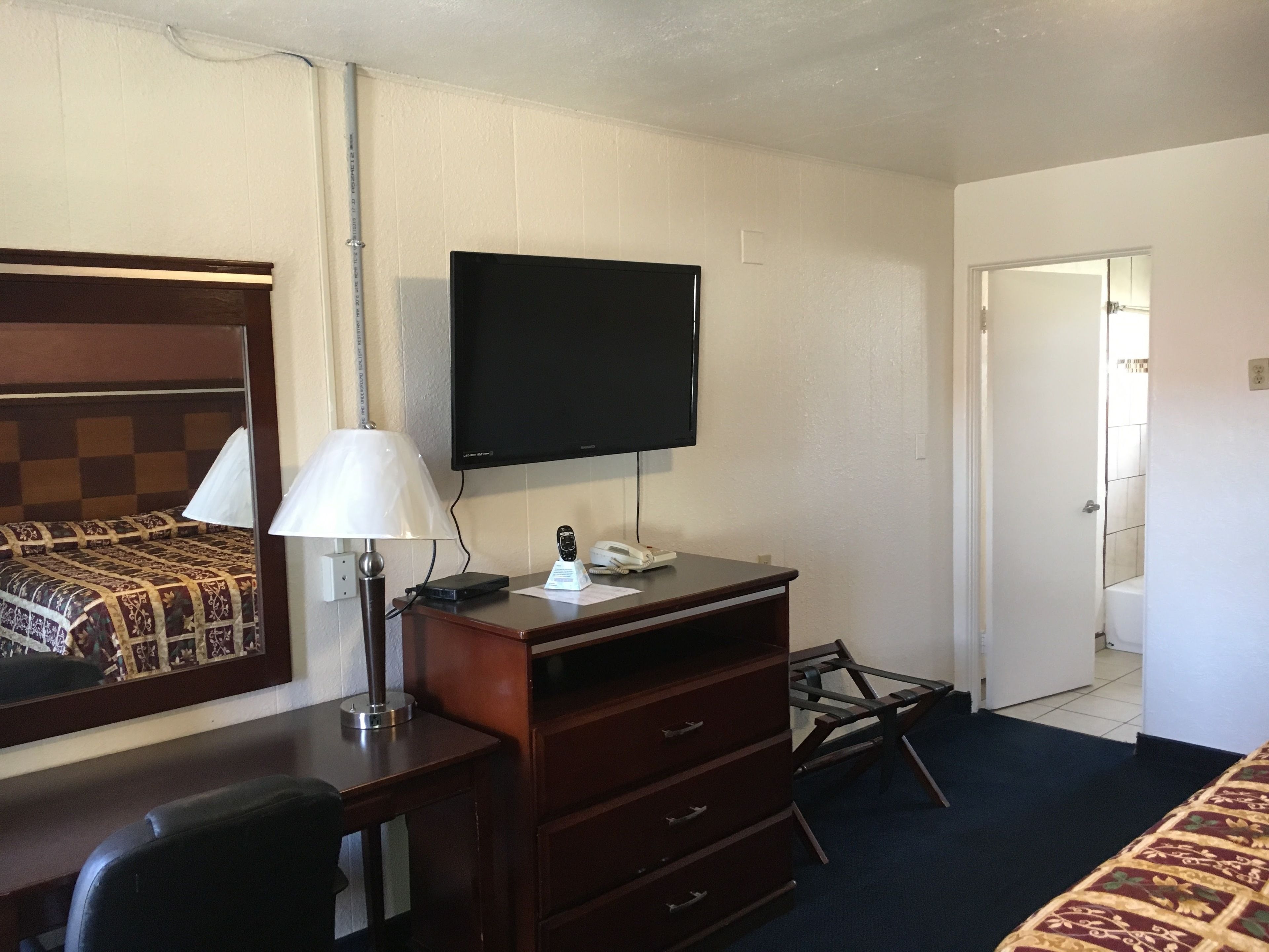Hotellihuone, jossa on sänky, työpöytä lampun kanssa, televisio ja lipasto.