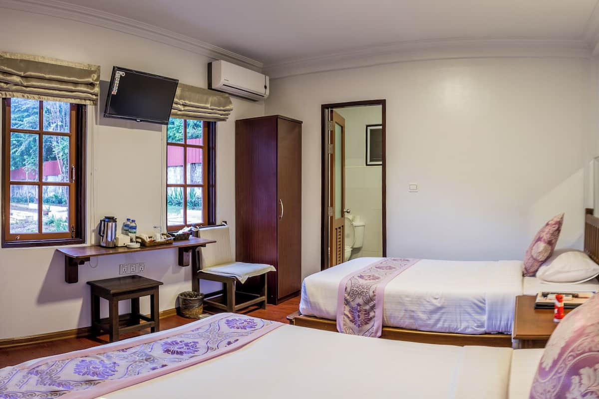 Habitación de hotel con dos camas, un escritorio, una silla, un televisor y una ventana con vistas a zonas verdes.