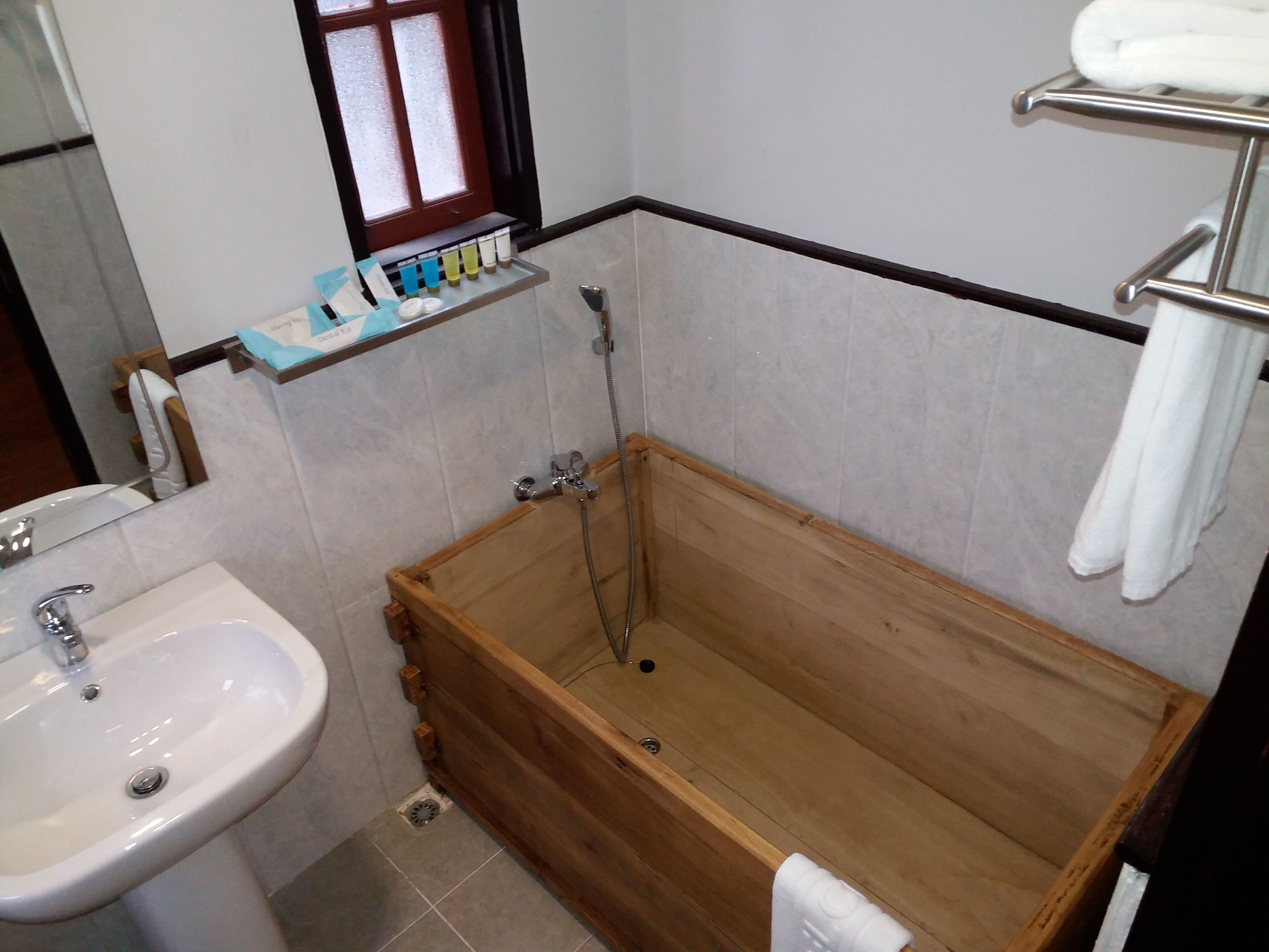 Un baño con una bañera de madera, un lavamanos blanco y una ventana con un estante encima.