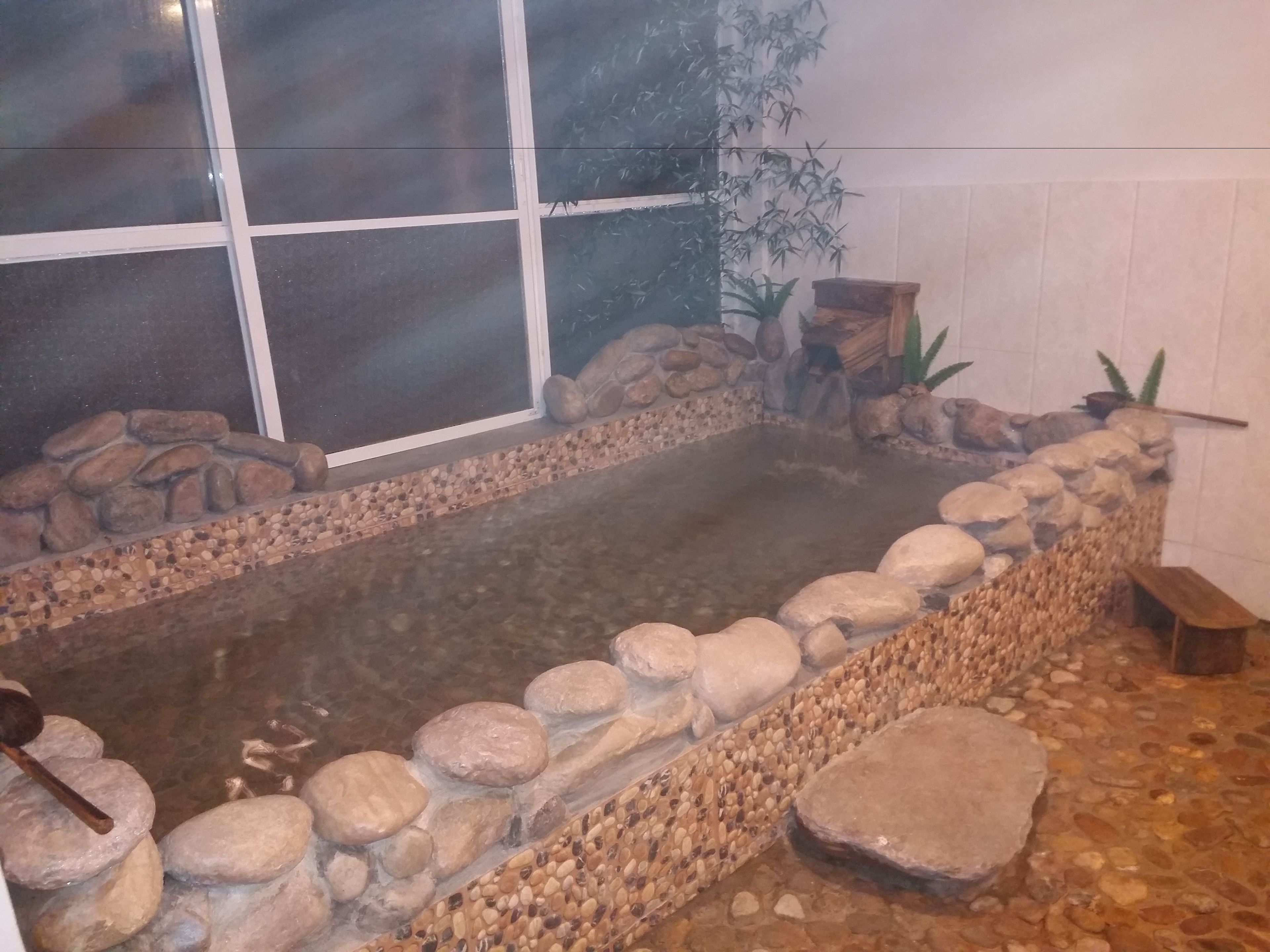 A hot tub with a stone border and a window in the background.