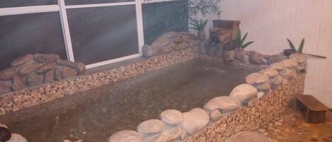 A hot tub with a stone border and a window in the background.