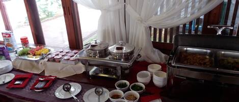 A buffet setup with various food items, including fruits, vegetables, and sauces, arranged on a table with plates and cutlery.