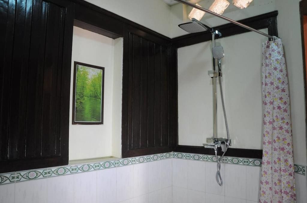 Een badkamer met donker houten lambrisering, een douche met een handdouche en een douchegordijn met een patroon.
