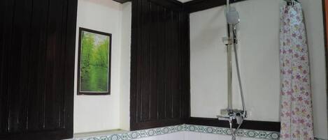 Un baño con paneles de madera oscura, ducha con cabezal de ducha manual y cortina de ducha estampada.