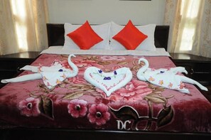 A bed with a floral bedspread, two red pillows, and a heart-shaped towel arrangement. - Hsaung Thazin Hotel Pyin Oo Lwin (Pyin Oo Lwin)