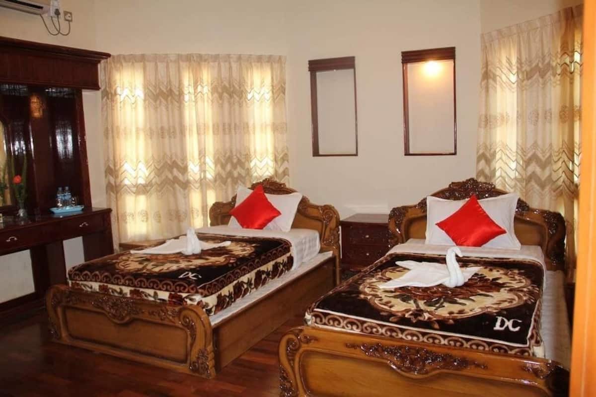 Quarto de hotel com duas camas de madeira, cada uma com colcha estampada e almofadas vermelhas.