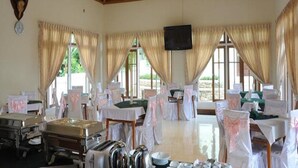A spacious dining area with multiple tables and chairs, large windows with curtains, and a flat-screen TV mounted on the wall. - Hsaung Thazin Hotel Pyin Oo Lwin (Pyin Oo Lwin)