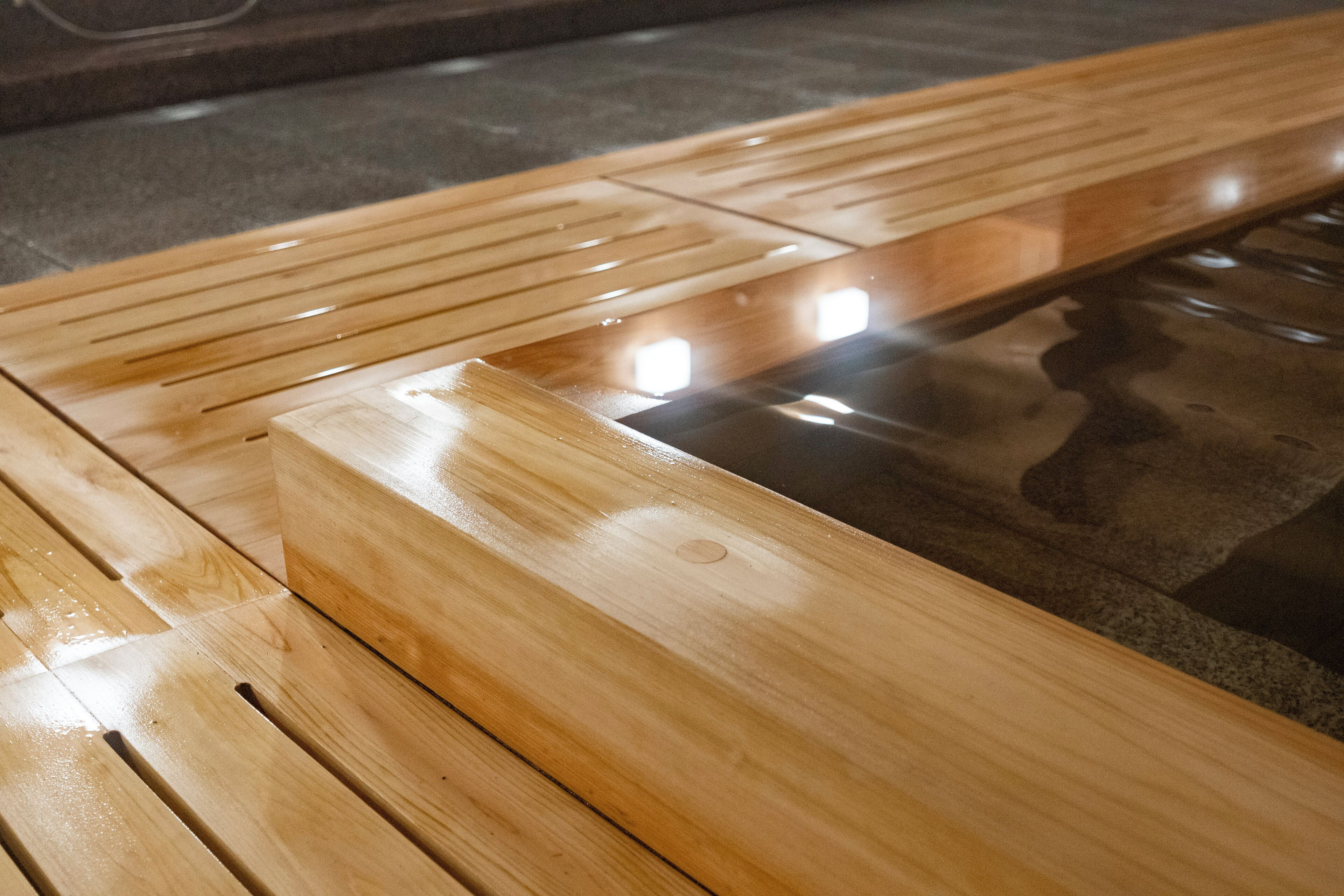 A wooden bench with a reflective surface, likely part of a public space or facility.