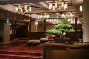 A lobby with a large bonsai tree, red carpeted stairs, and multiple chandeliers.