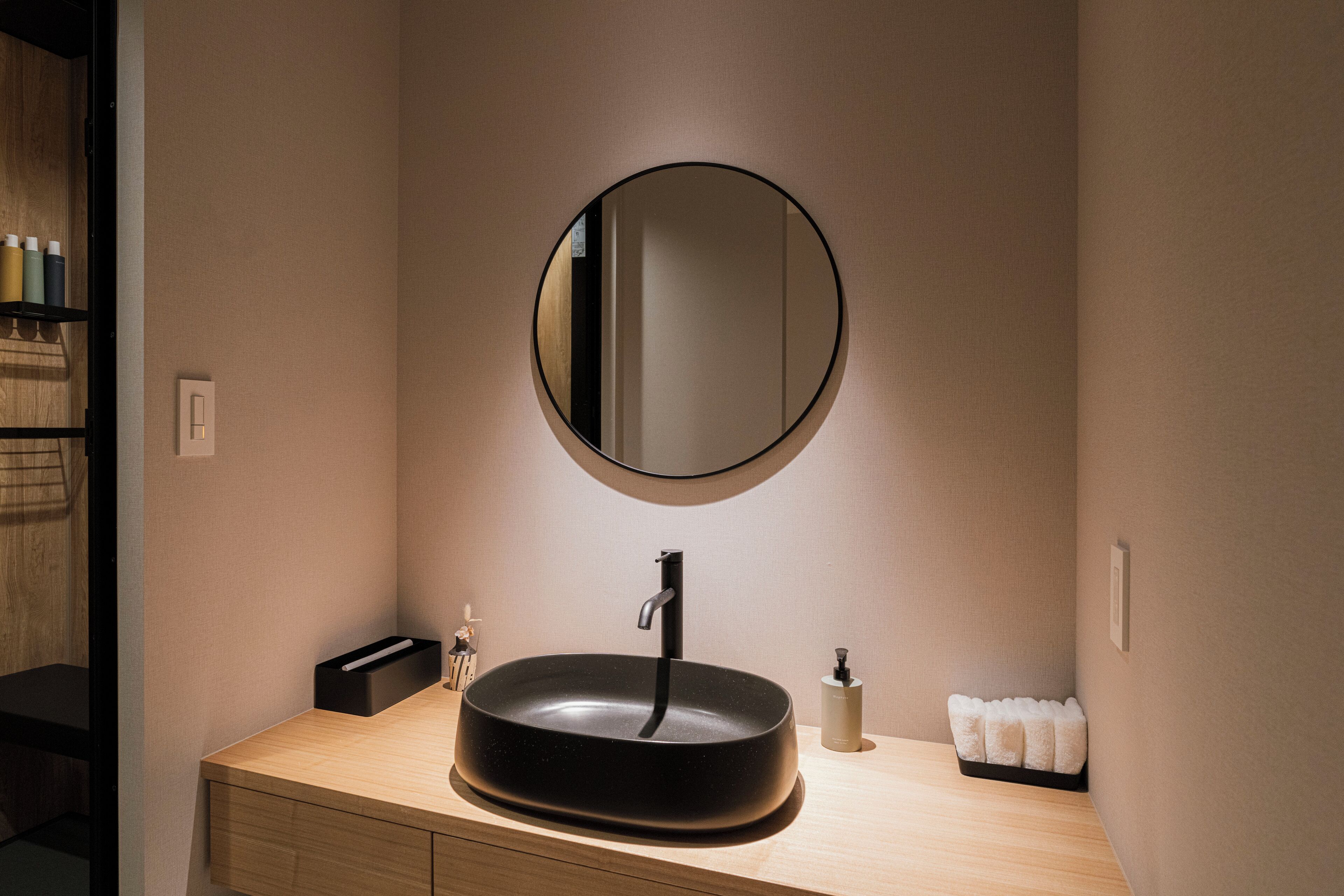 A modern bathroom with a round mirror, a black sink, and a wooden vanity.