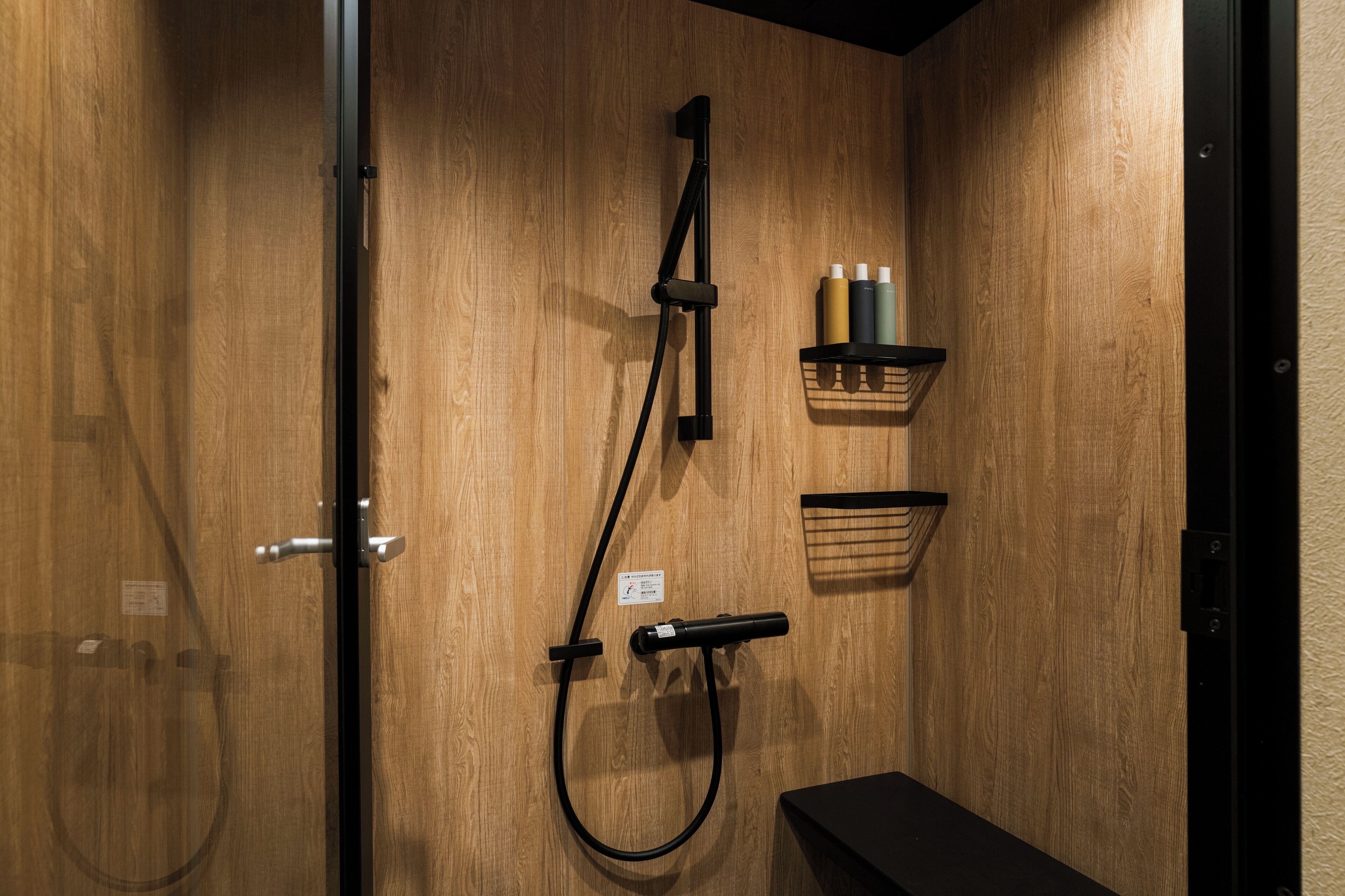 A wooden wall with a shower, a shelf with bottles, and a small basket.