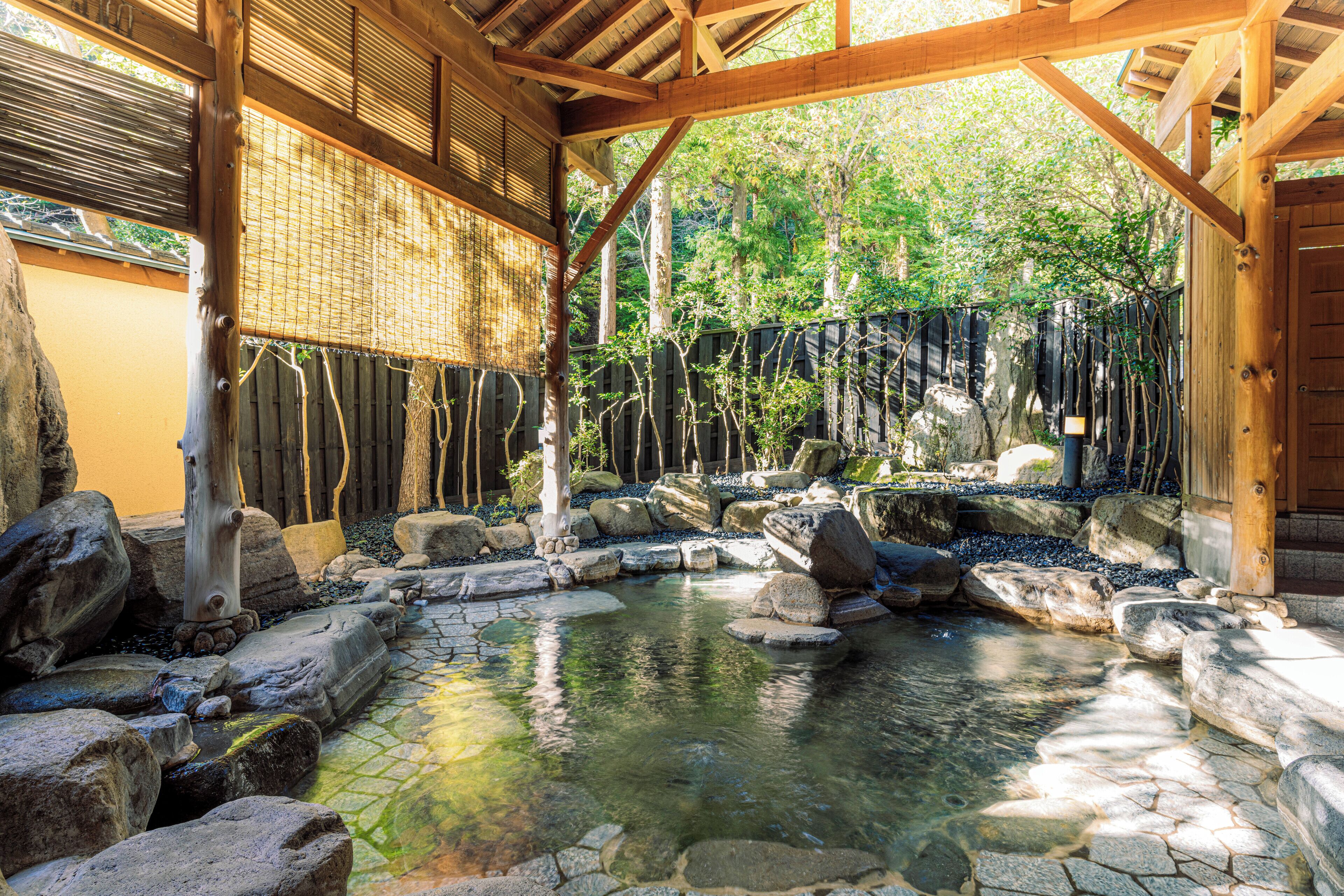 A traditional Japanese garden with a stone pond, wooden bridge, and bamboo fence.