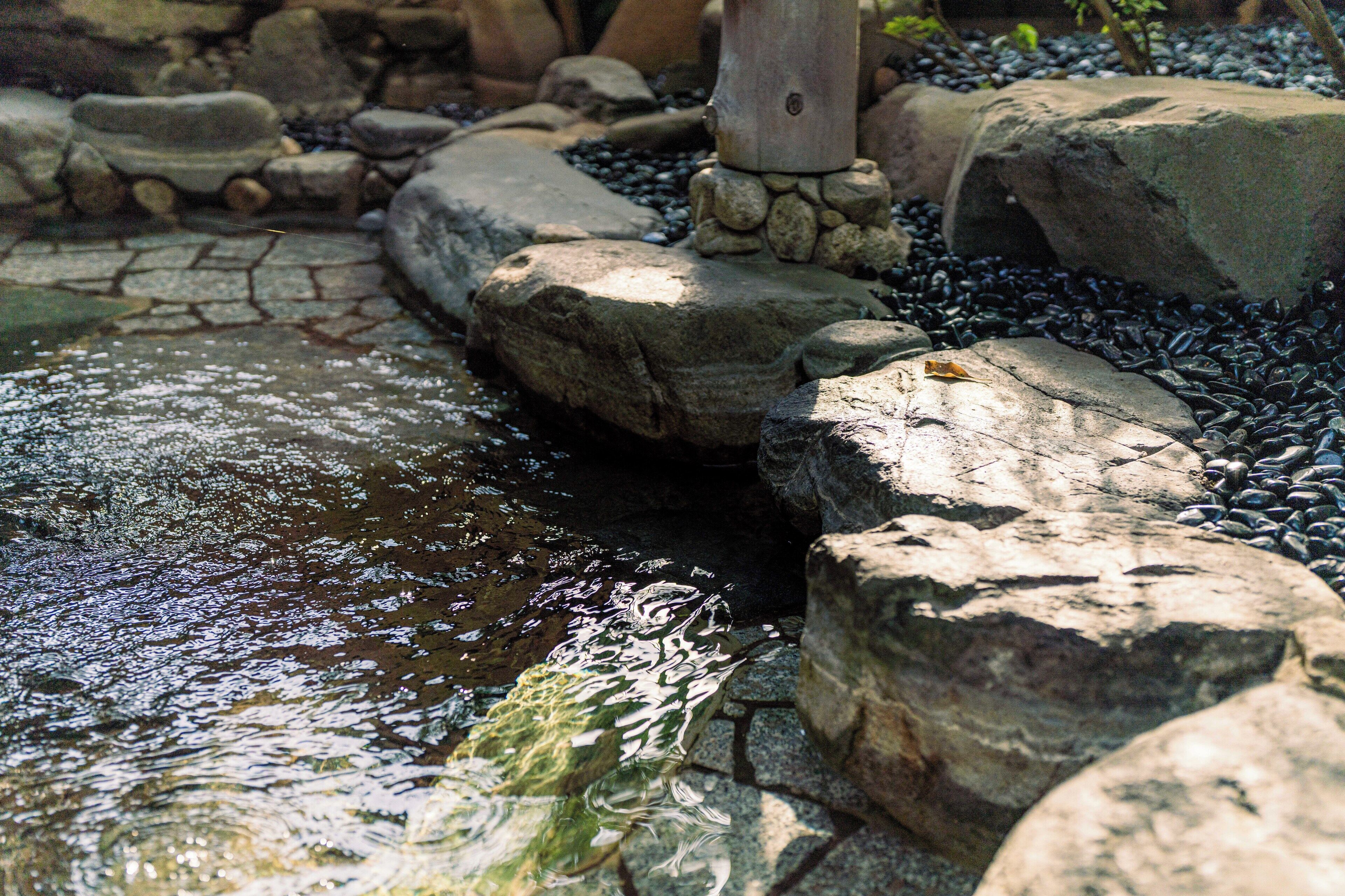 A stone water feature with a small stream, surrounded by rocks and pebbles.