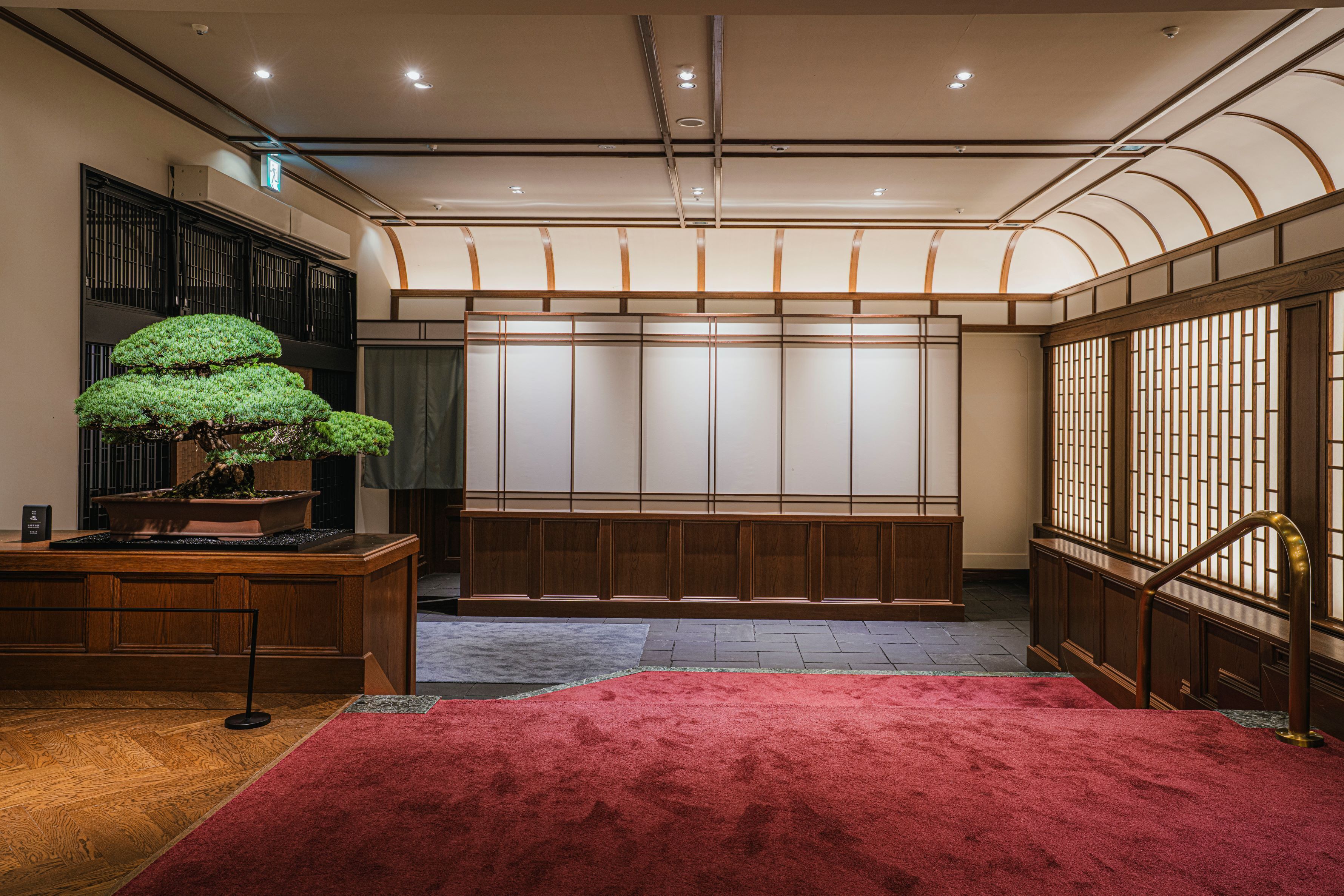 A traditional Japanese room with tatami flooring, a red carpet, and a bonsai tree.