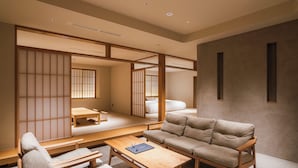 A traditional Japanese-style room with tatami flooring, a low wooden table, a sofa, and sliding doors. - Shinzan (Toyooka)