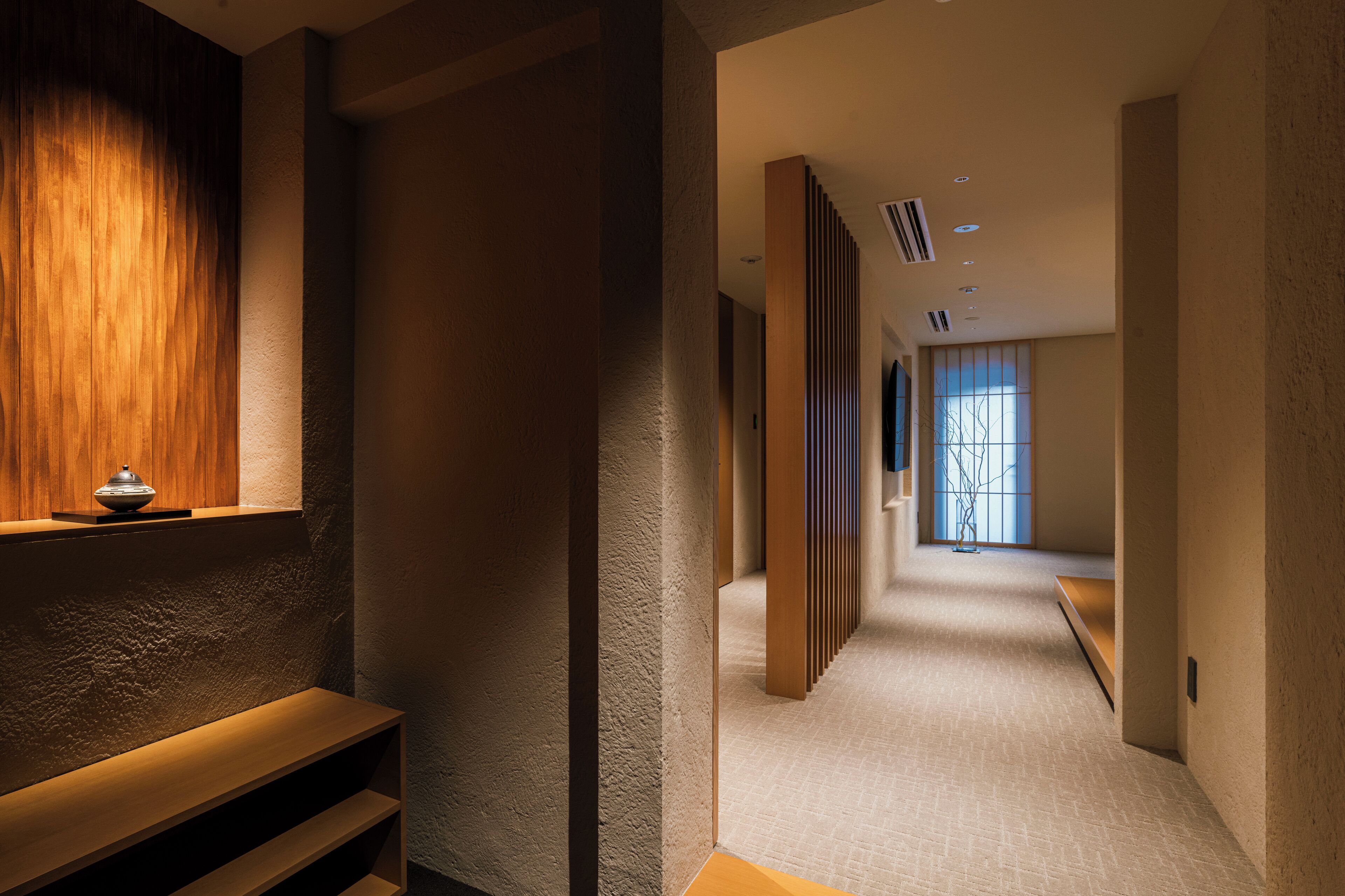 A hallway with a wooden bench, a textured wall, and a window with a view.
