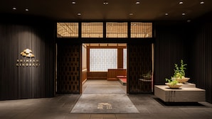 A traditional Japanese-style entrance with a wooden door, a reception desk, and a potted plant. - Shinzan (Toyooka)