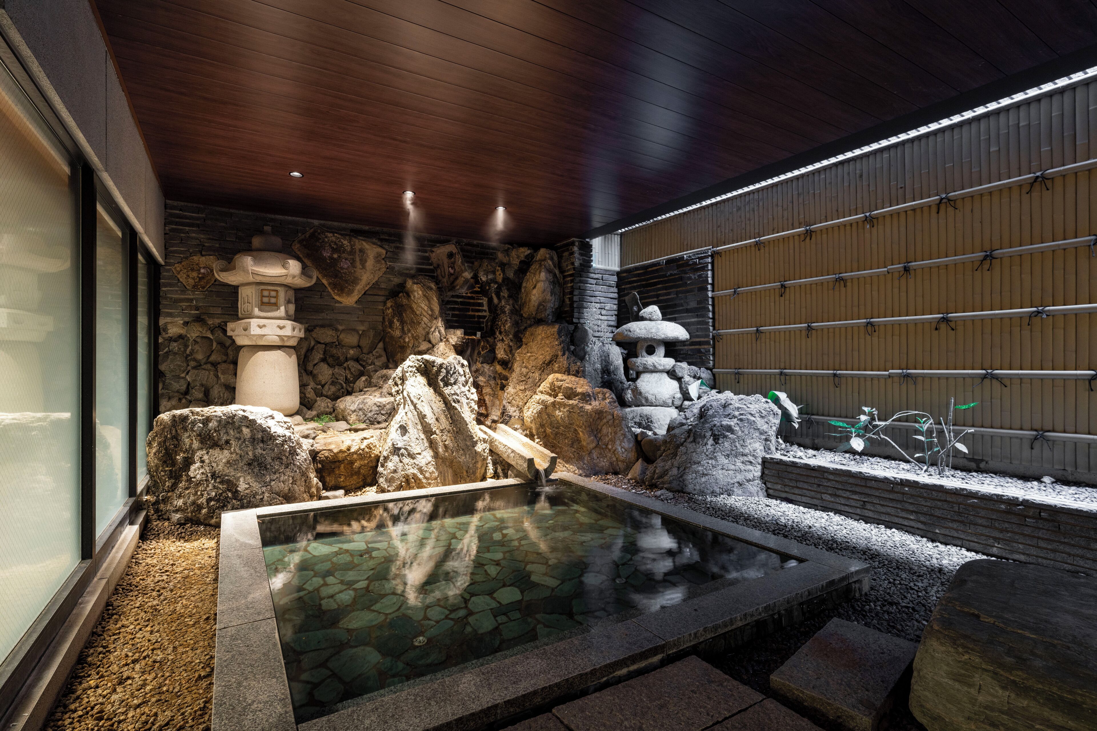 A modern spa area with a hot spring, stone walls, and a wooden ceiling.