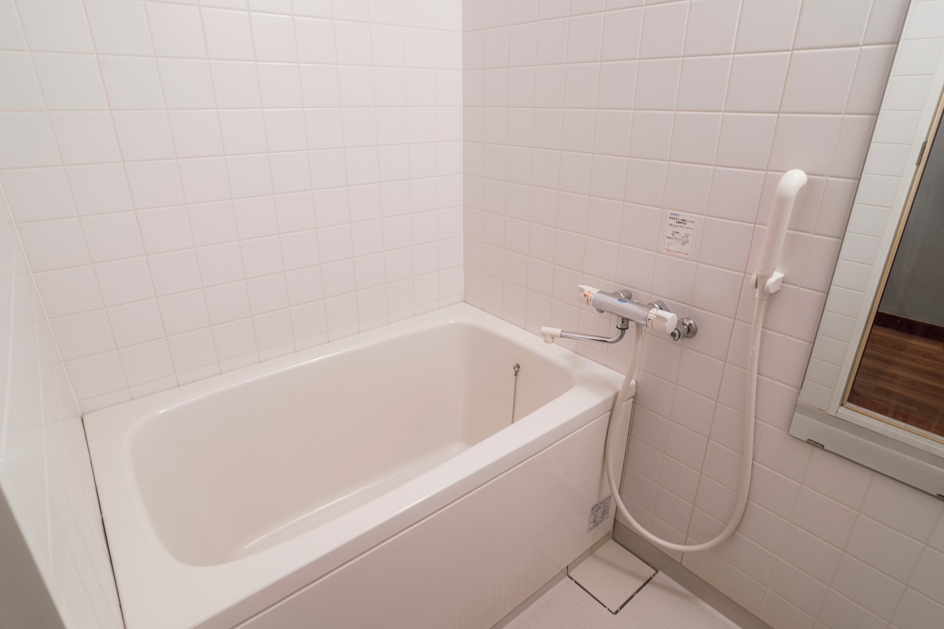 A white bathtub with a shower attachment, a small window, and a tiled wall.