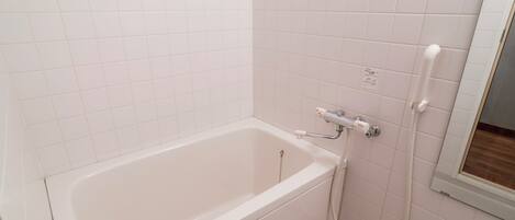 A white bathtub with a shower attachment, a small window, and a tiled wall.