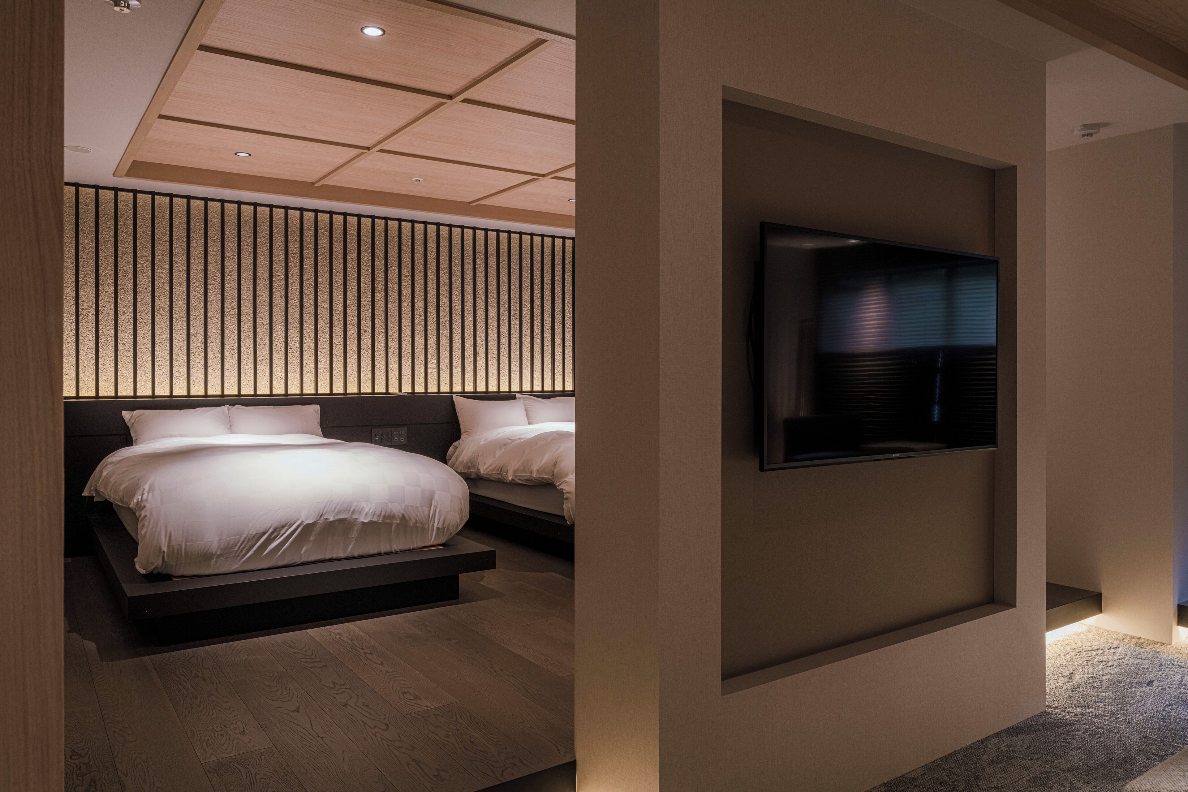 Una camera da letto moderna con due letti, una TV integrata e un pannello parete in listelli di legno.