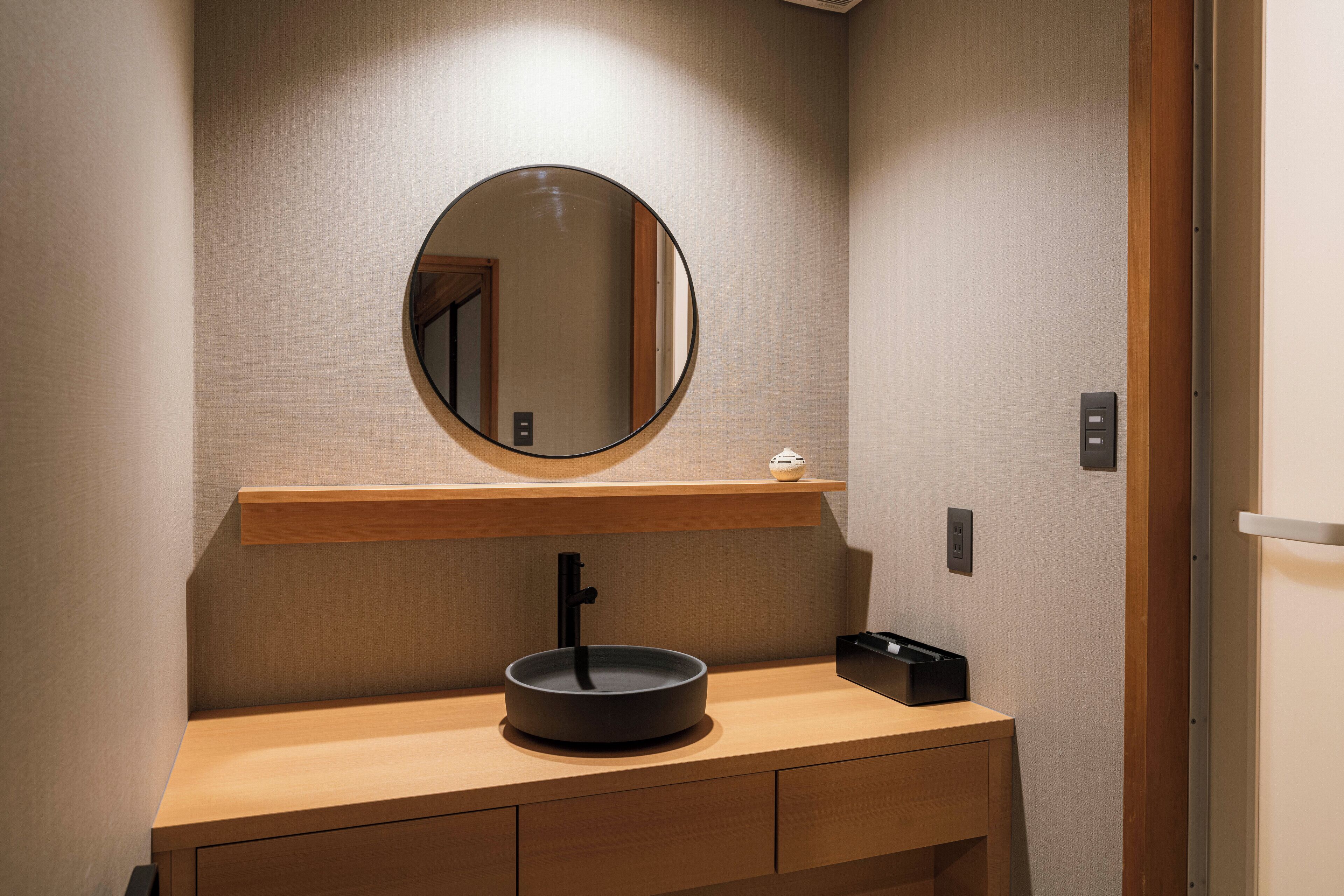 A bathroom with a round mirror, a wooden vanity, and a black sink.