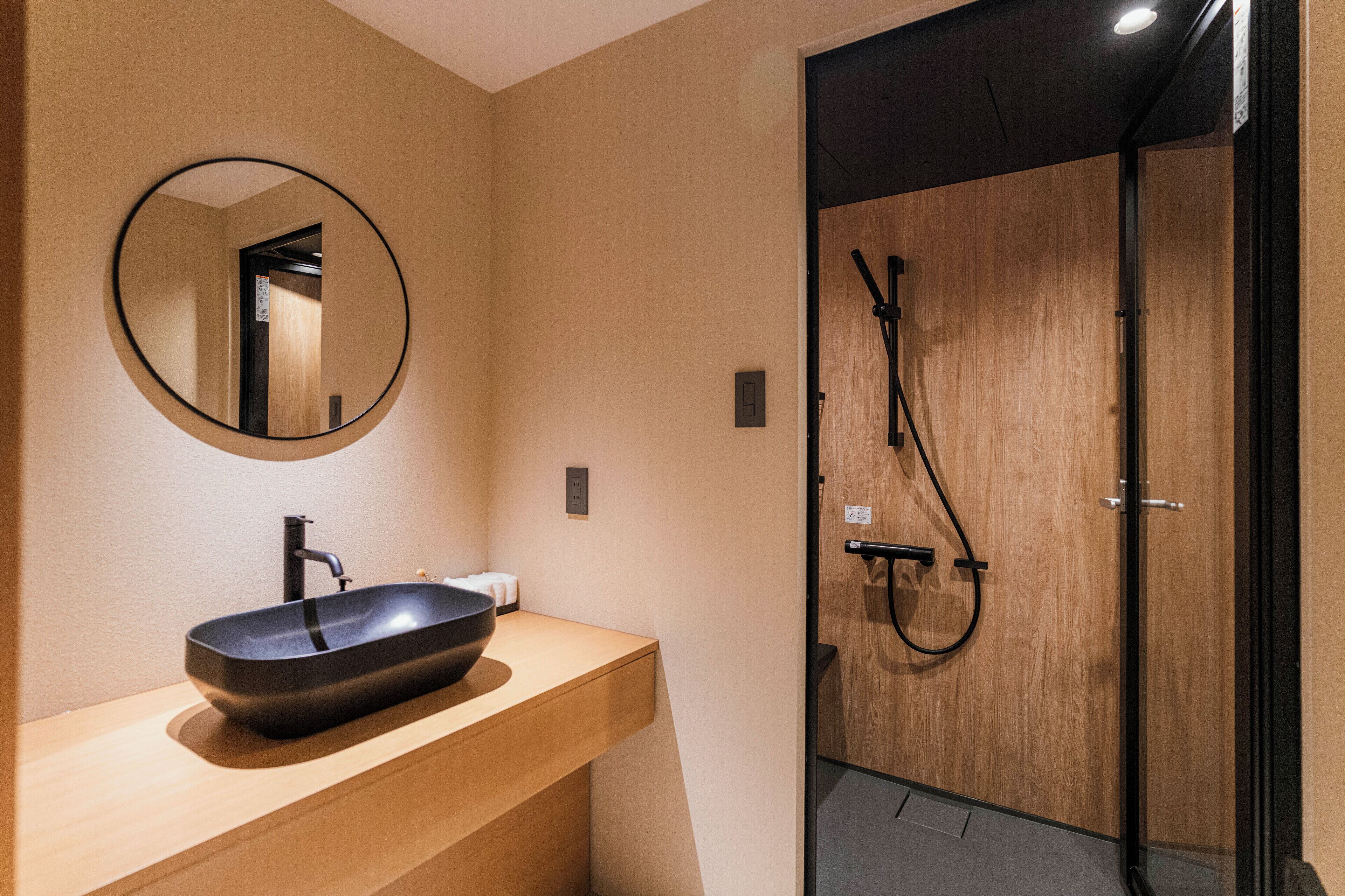 A modern bathroom with a round mirror, a black vessel sink, and a glass-enclosed shower area.