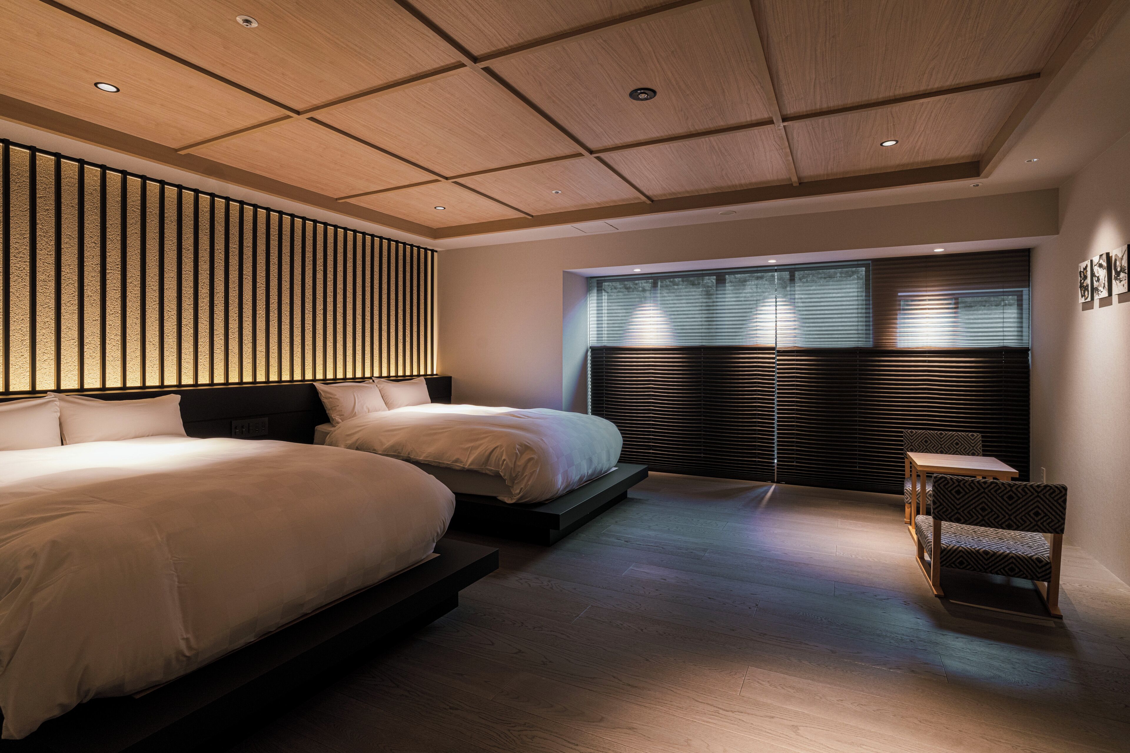 A modern bedroom with two beds, a wooden ceiling, and a window with blinds.