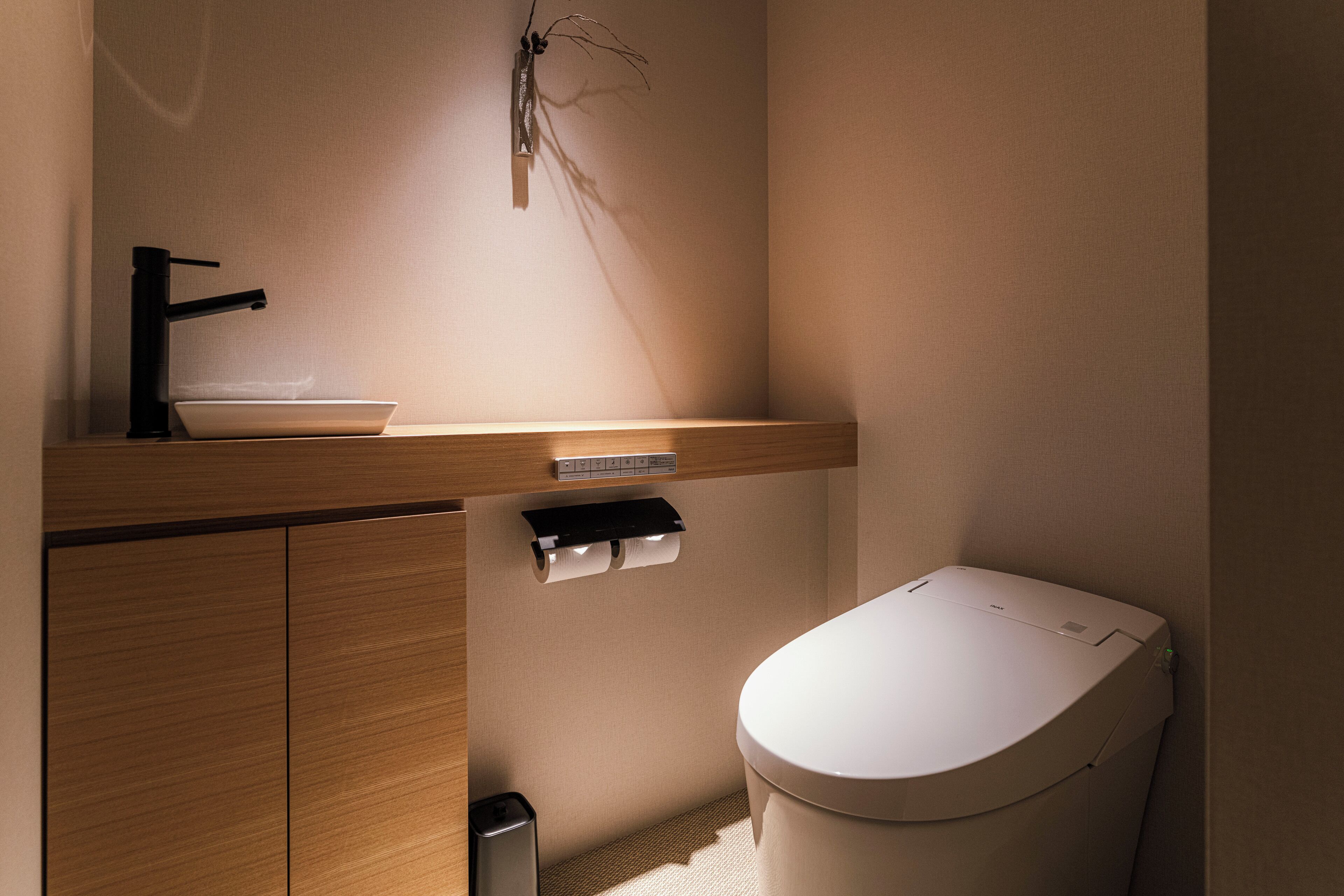 A modern bathroom with a wooden vanity, a white toilet, and a black faucet.