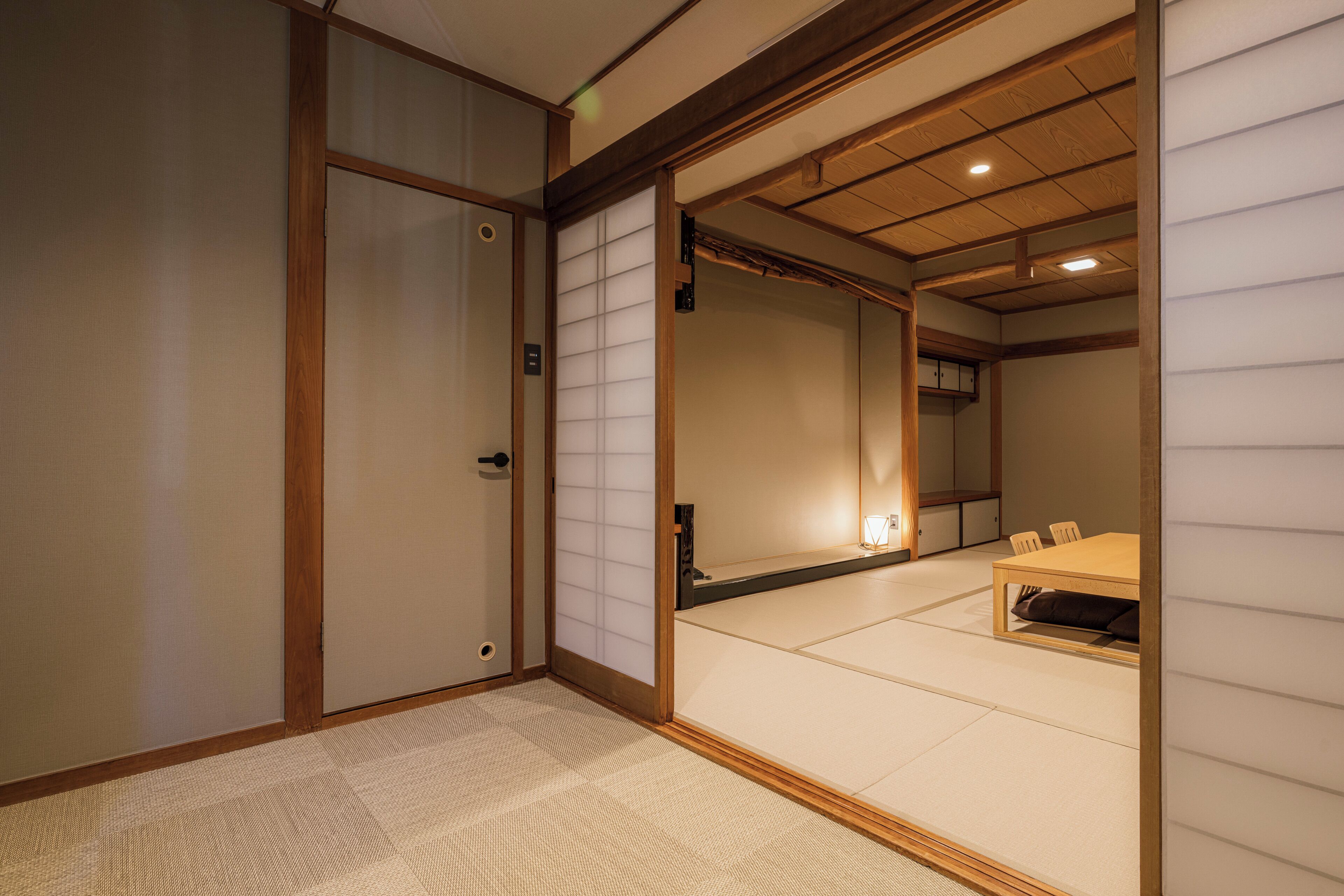 Ein traditioneller japanischer Raum mit Tatami-Boden, einer Schiebetür und einem niedrigen Holztisch mit Stühlen.